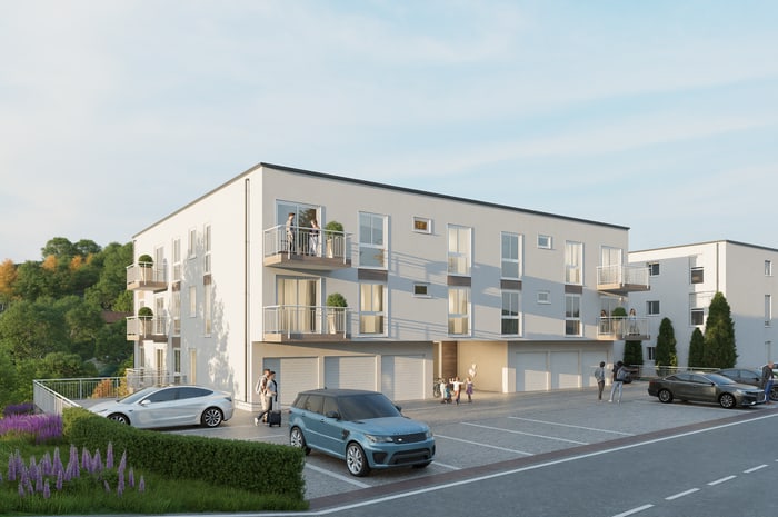 Modernes Mehrfamilienhaus mit weißen Fassaden, Balkonen und Parkplätzen davor.