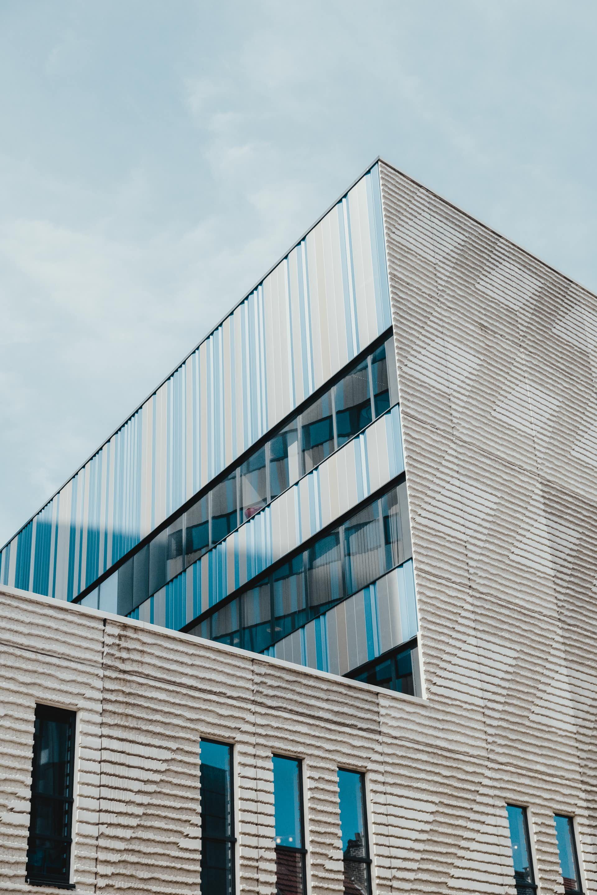 Moderne Gebäudefassade mit schräger Glasfront vor blauem Himmel